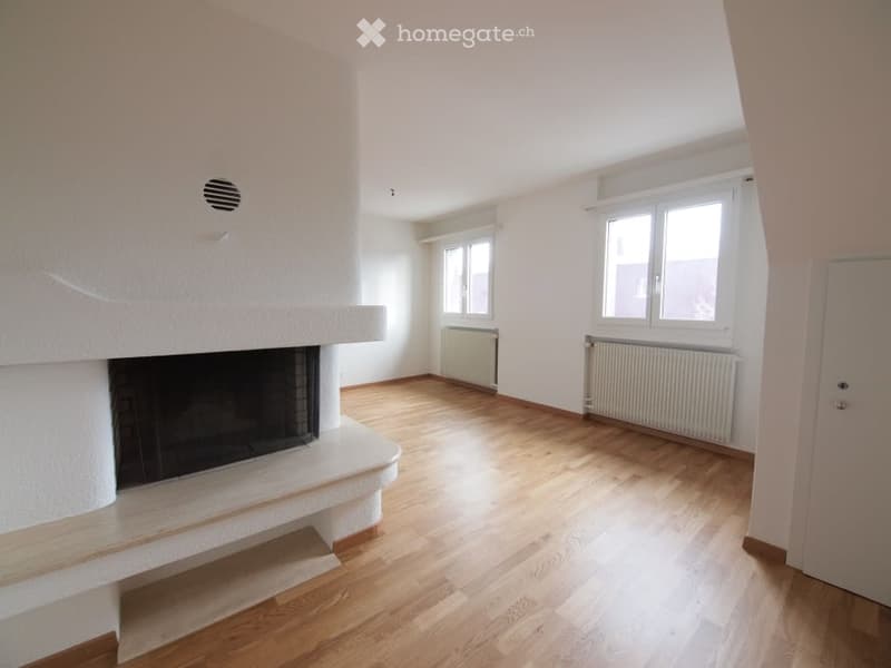 Empty room with wooden flooring, white walls, fireplace, and two windows with radiators beneath them.