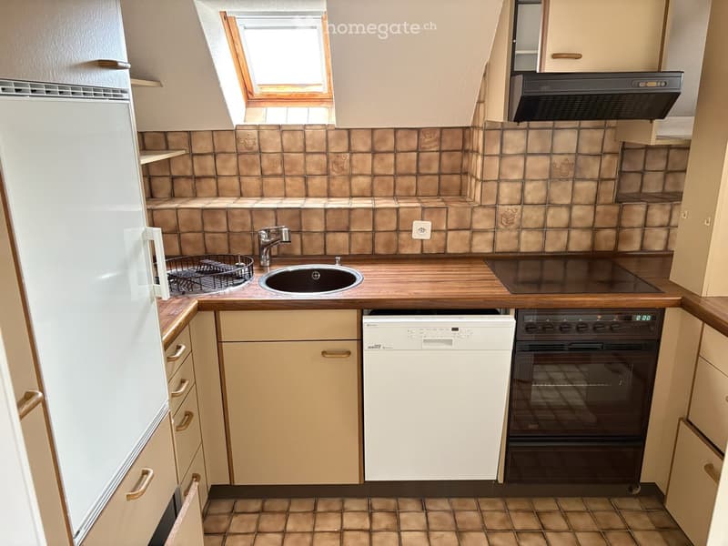 Compact kitchen with wooden countertops, beige cabinets, a sink, a refrigerator, a dishwasher, and an oven. The backsplash features brown tiles, and the floor is tiled.