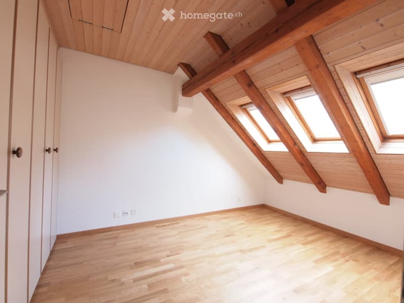 Empty attic room with wooden floors, white walls, exposed wooden beams, and skylight windows.