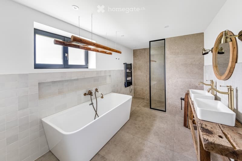 Modern bathroom with a freestanding bathtub, double sinks, and a large mirror. Features include a wooden shelf, a window, and a glass shower enclosure.