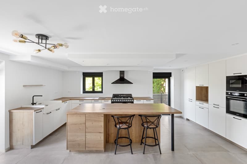 Modern kitchen with white cabinets, wooden island, stainless steel appliances, and two bar stools.