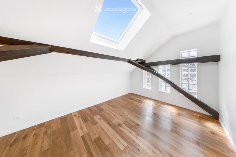 Empty attic space with wooden floors, white walls, exposed wooden beams, and skylight windows.
