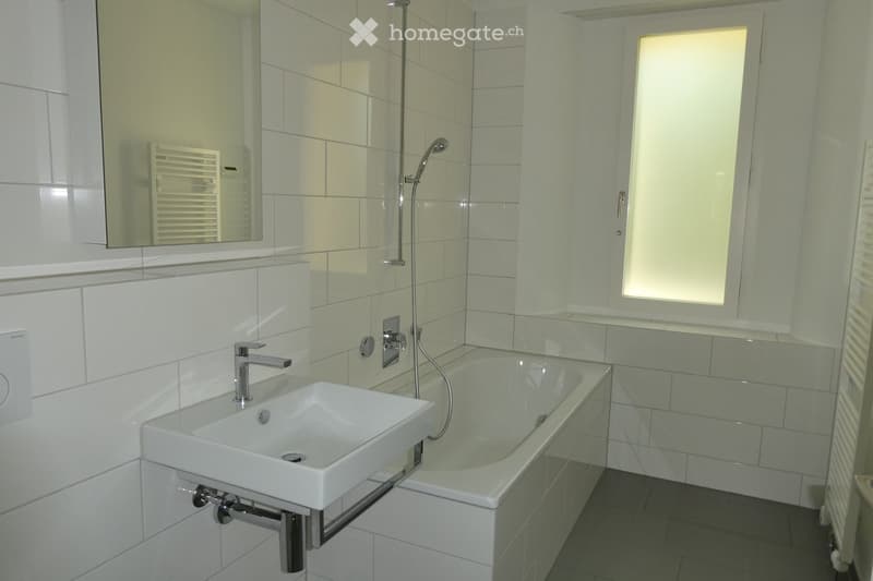 Modern bathroom with white tiles, a sink, bathtub, mirror, and showerhead.