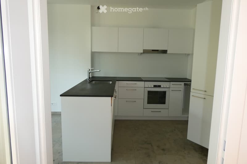Modern kitchen with white cabinets, black countertop, stainless steel sink and faucet, built-in oven, and tiled floor.