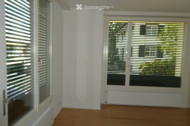 Empty room with white walls, wooden floor, and large windows with blinds. No furniture or equipment present.