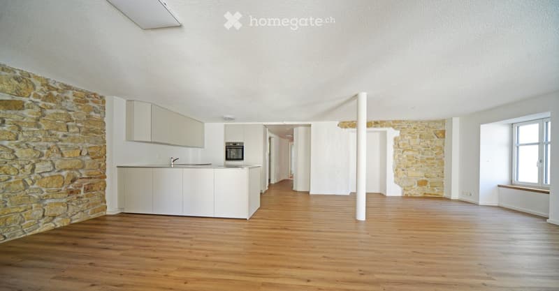 Open-plan kitchen and living area with light wooden flooring, white cabinets, and a stone accent wall.
