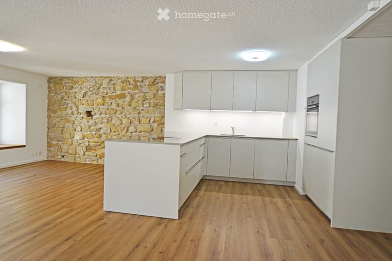 Modern kitchen with white cabinets, a stone accent wall, and wooden flooring.