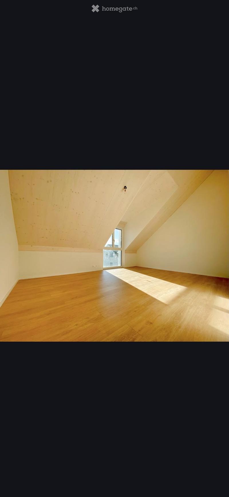 Empty attic room with wooden flooring, slanted wooden ceiling, and a single window letting in natural light.