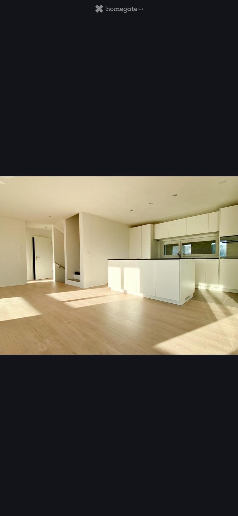 Modern kitchen with white cabinets, a central island, and light wooden flooring. The space is well-lit with natural light streaming in from the windows.