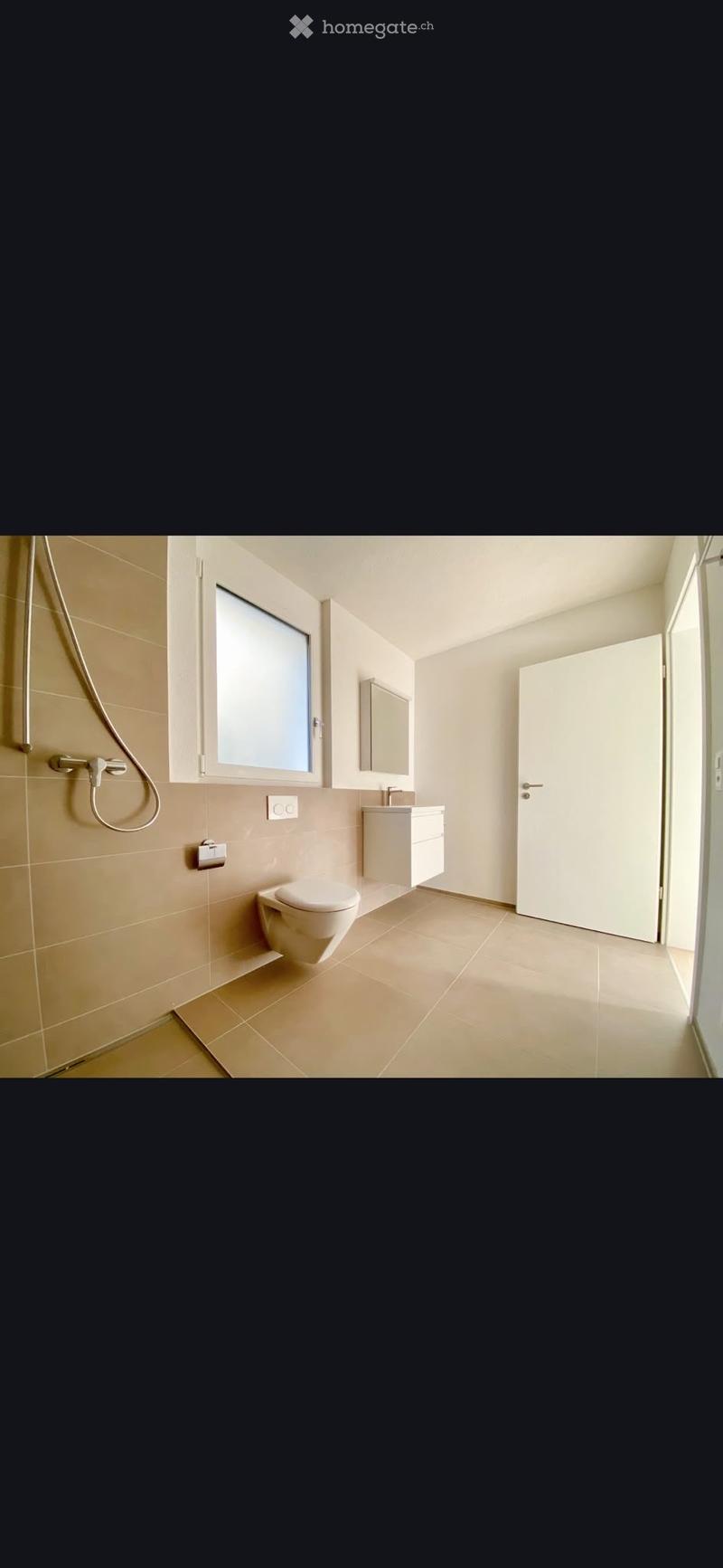 Modern bathroom with beige tiles, a toilet, a sink with a mirror, and a shower hose on the wall.