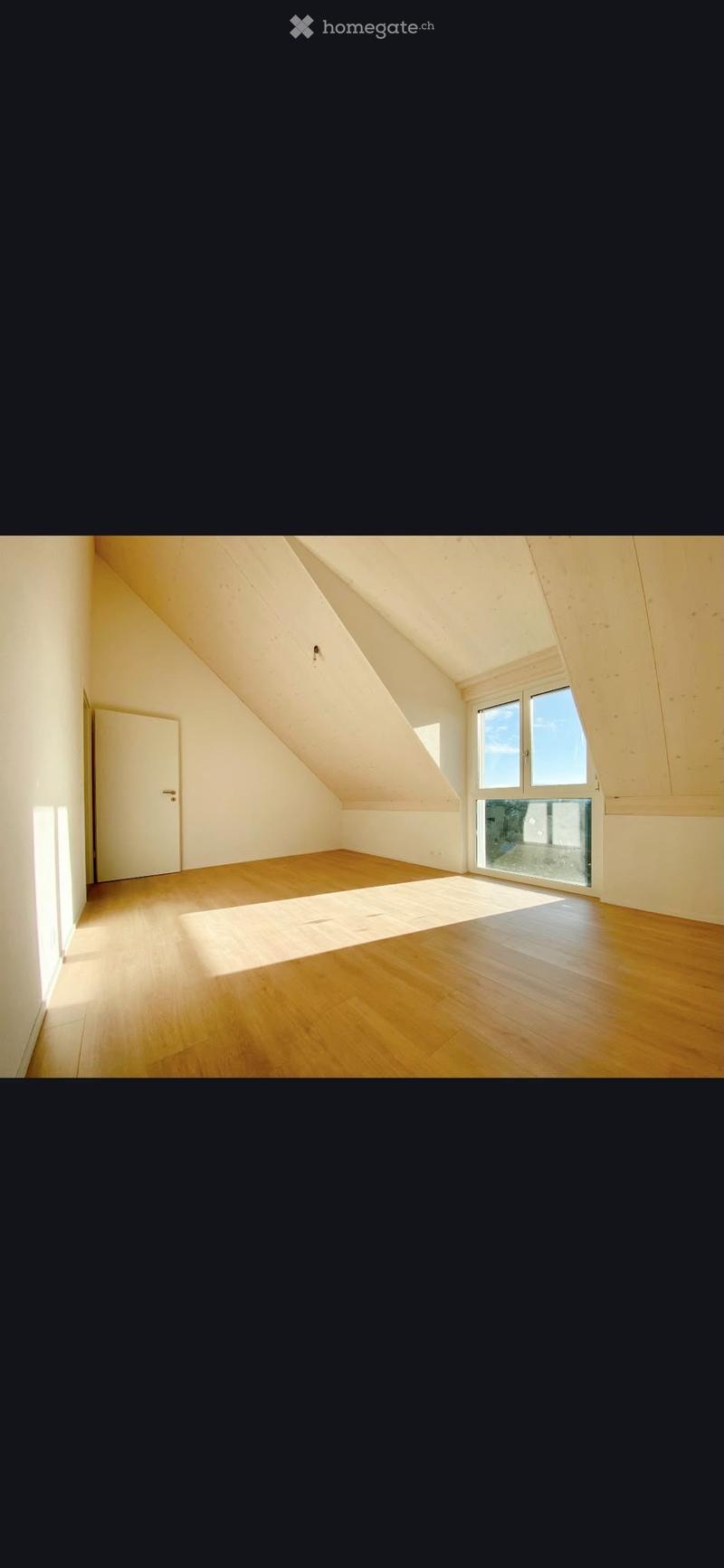 Empty attic room with wooden flooring, white walls, and large windows allowing natural light to enter.