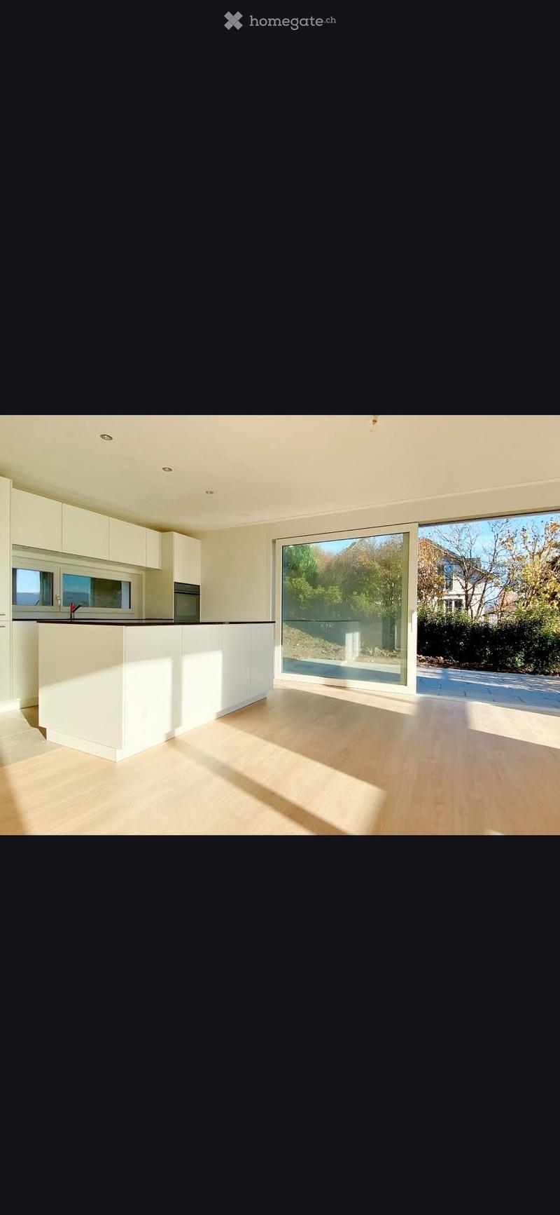 Modern, minimalist kitchen with white cabinets, a central island, and large windows overlooking a garden area.