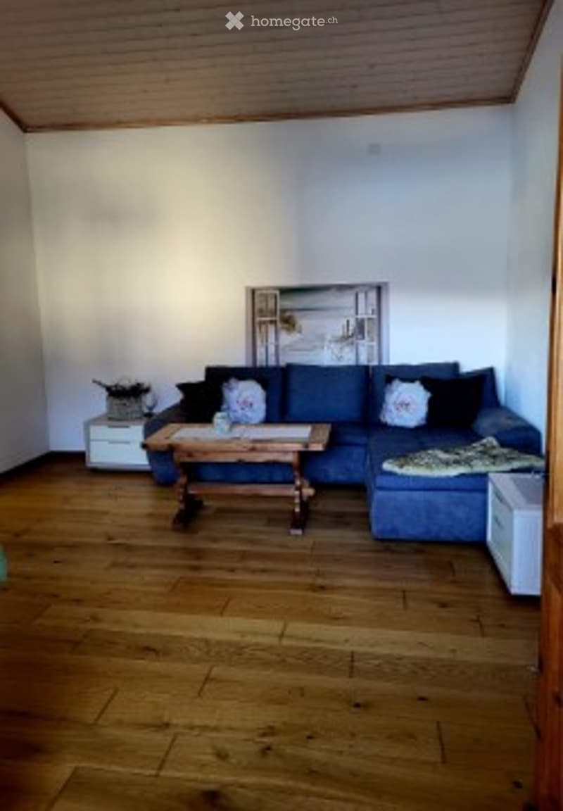 Bright living room with wooden flooring, blue sectional sofa, wooden coffee table, side table, throw blanket, and decorative pillows.
