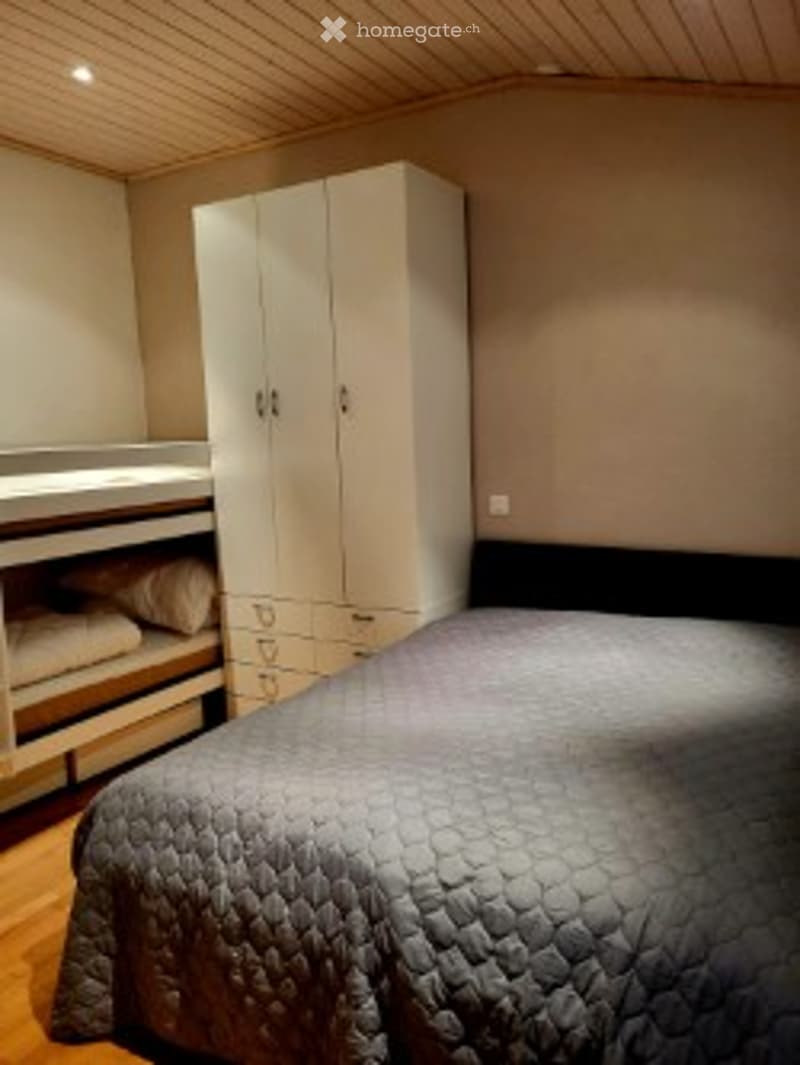 Cozy bedroom with a double bed, quilted duvet, white wardrobe, nightstand, and warm lighting.