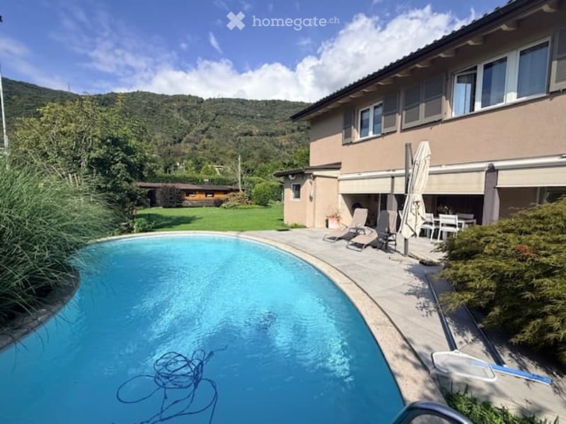 Private outdoor area with a swimming pool, lounge chairs, and a dining set under umbrellas, surrounded by greenery and a scenic mountain view.