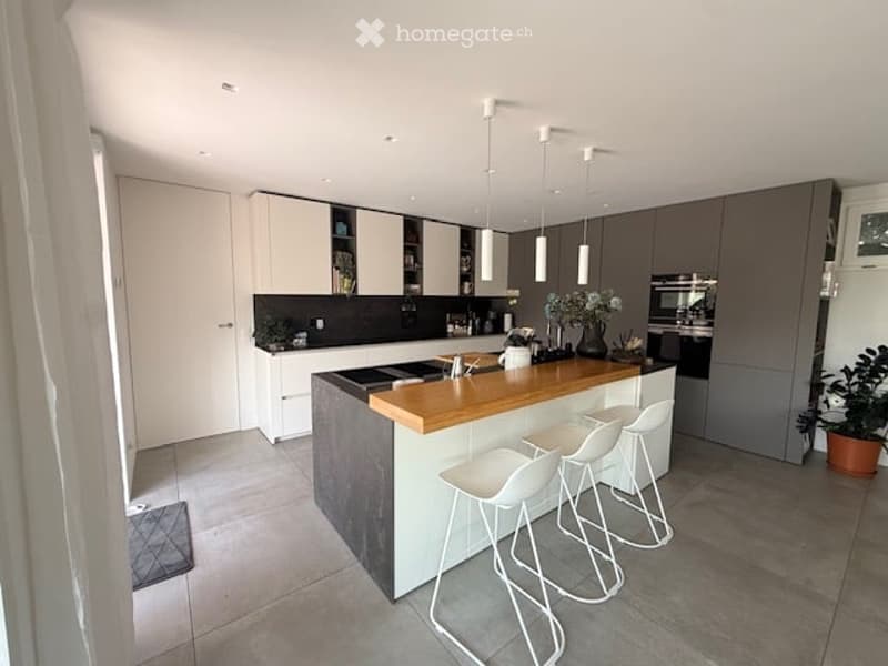 Modern kitchen with white and grey cabinetry, a wooden countertop island, white bar stools, and built-in appliances including an oven and sink.