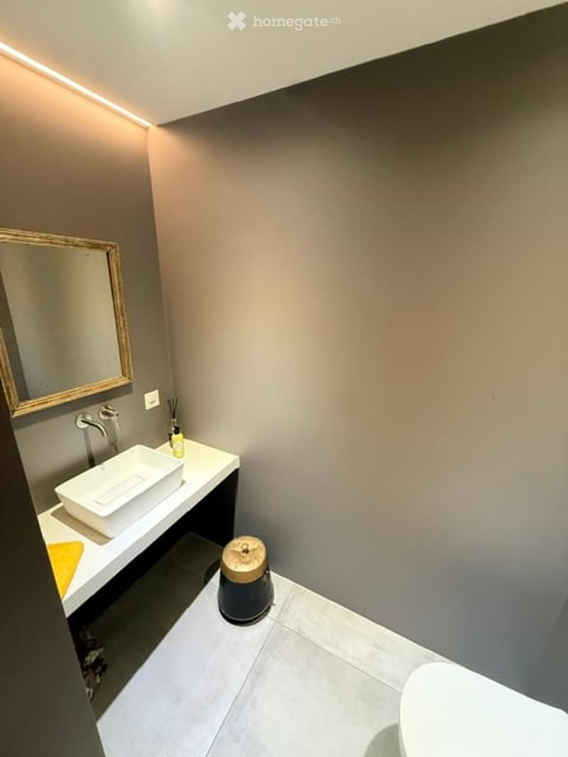 Modern bathroom with a white sink, gold-framed mirror, sleek faucet, and a small round stool near the sink.