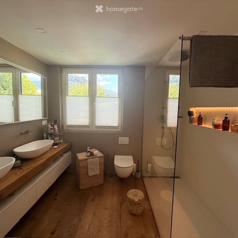 Modern bathroom with wooden flooring, double sink vanity, large windows offering a scenic view, a toilet, a bathtub, and a shower area with glass enclosure.