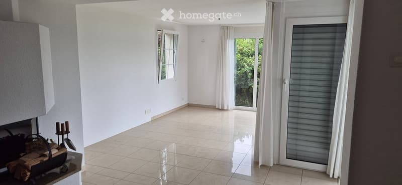 Empty room with white walls, tiled floor, and large windows with white curtains. A sliding glass door leads to an outdoor area.