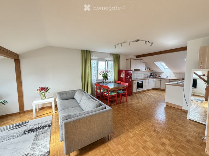 Open-plan living and dining area with a grey sofa, coffee table, dining table with chairs, and a red refrigerator in the kitchen area.