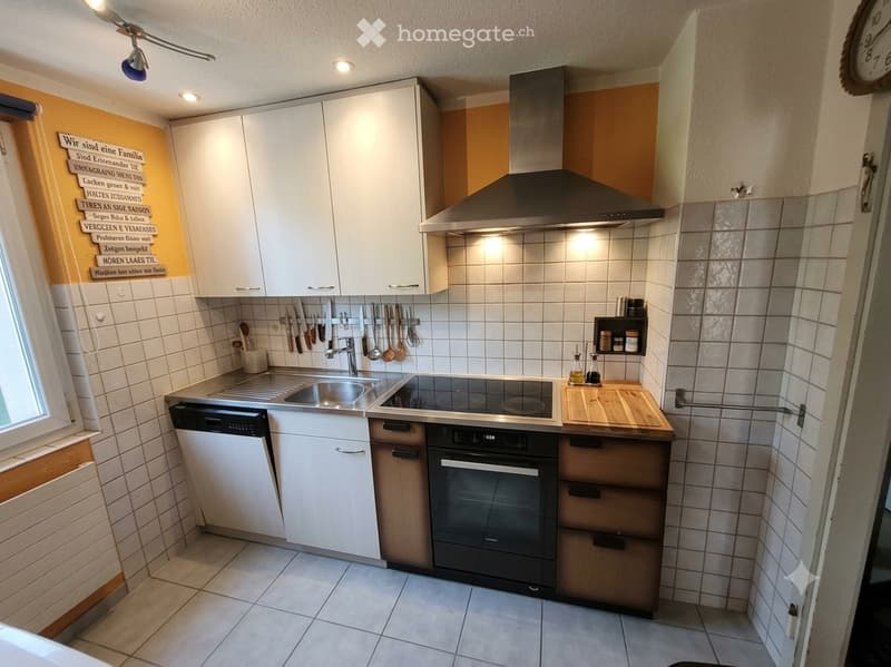 Modern kitchen with white cabinets, stainless steel appliances, tiled walls, and a wooden cutting board on the counter.