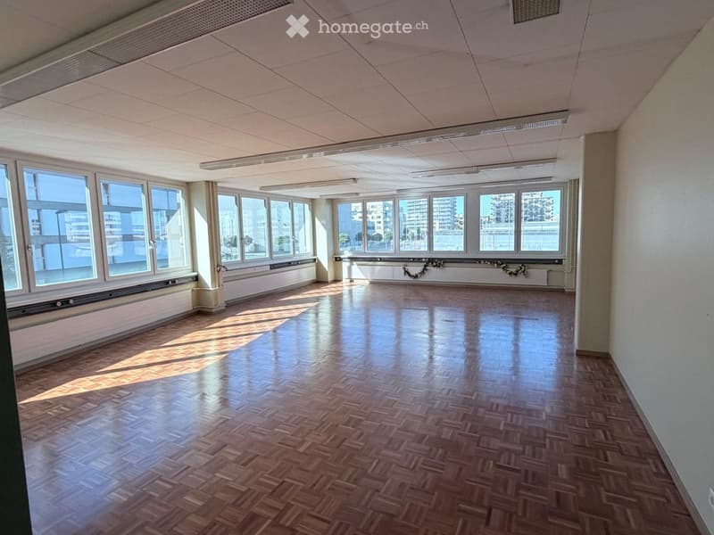 Empty room with wooden flooring and large windows offering a view of the cityscape.