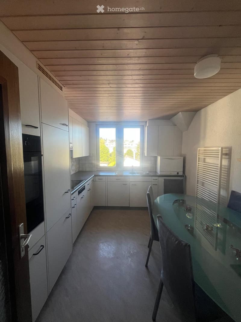 Modern kitchen with white cabinets, stainless steel appliances, a central island, and a dining area with a glass table and chairs.