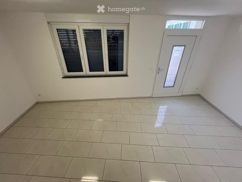 Empty room with tiled floor, white walls, large window with blinds, and a white door with glass panel.