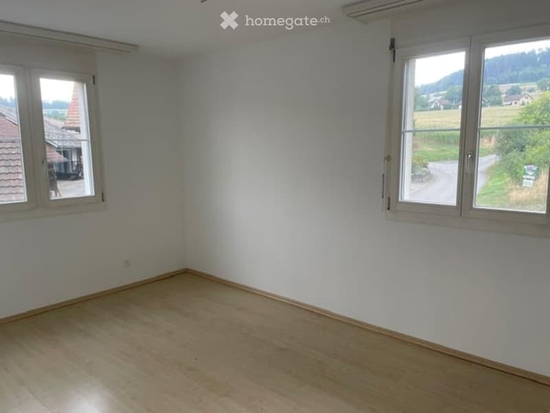 Empty room with wooden flooring and white walls, featuring large windows with a scenic countryside view.