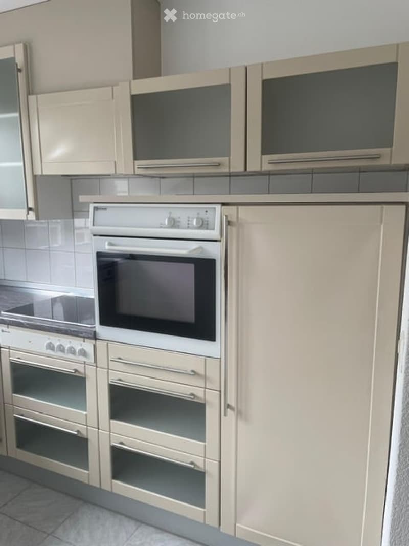 Modern kitchen with light-colored cabinets, built-in oven, microwave, and tiled backsplash.