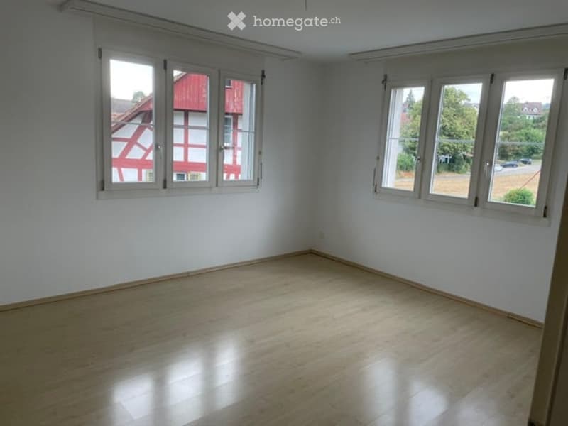 Empty room with wooden flooring and white walls, featuring large windows with white frames and blinds. No furniture or equipment present.