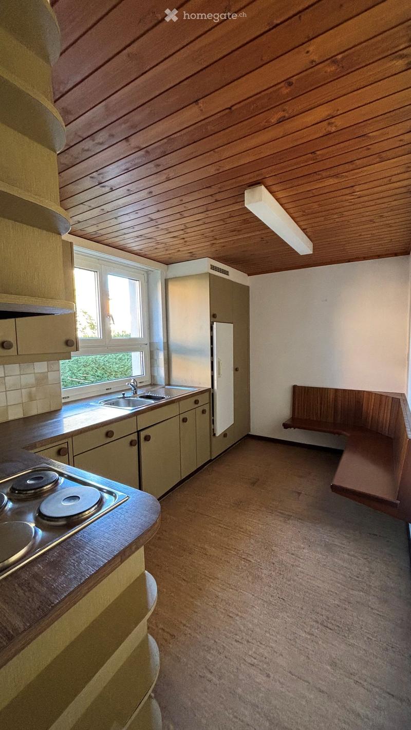 Kitchen with wooden ceiling, light-colored cabinets, a refrigerator, a sink, a bench, and a stove.