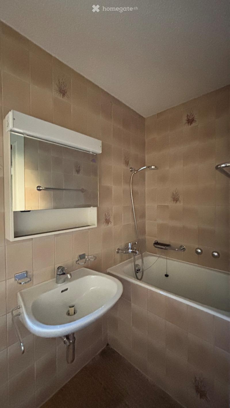 Bathroom with beige tiled walls and floor, featuring a white sink, bathtub, mirror, and showerhead.