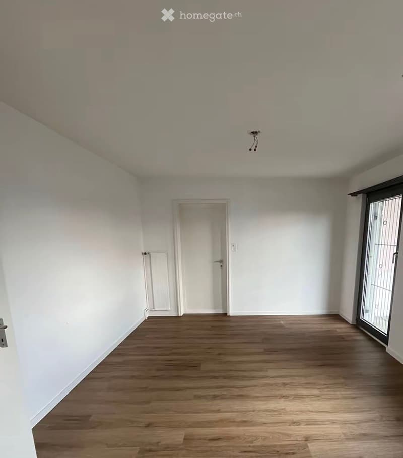 Empty room with wooden flooring, white walls, a door, and a radiator. No furniture or equipment present.