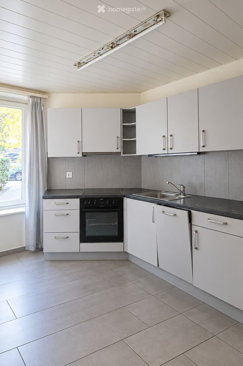 Modern kitchen with white cabinets, stainless steel sink, and built-in oven. Grey tiled backsplash and light grey tiled floor.
