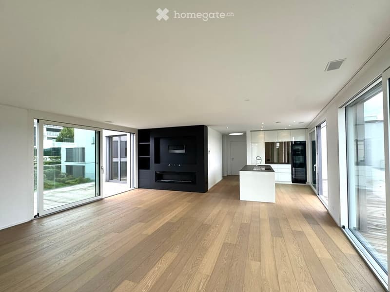 Open-plan living and dining area with light wooden flooring, large glass sliding doors leading to a balcony, a modern kitchen island with a sink, and a built-in fireplace unit.