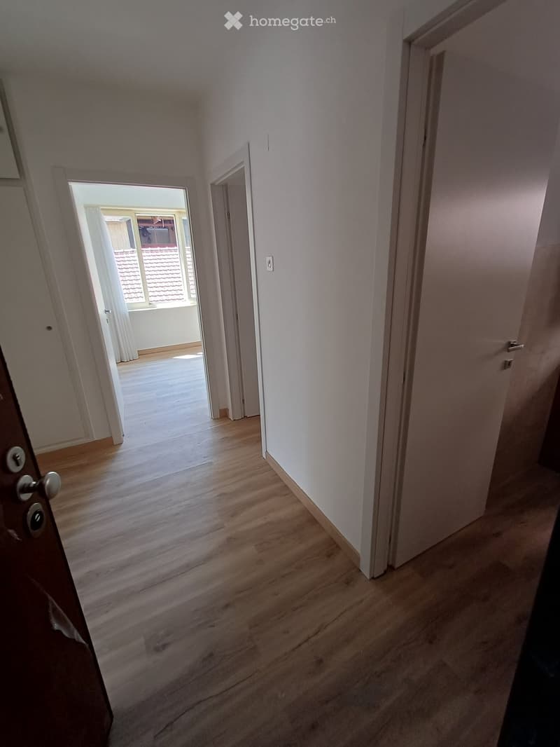 Empty hallway with wooden flooring, white walls, and doors leading to other rooms and a balcony area.