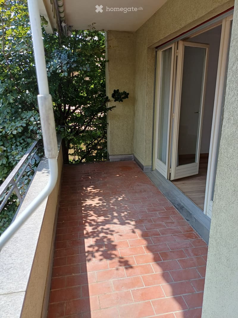 Balcony with red tiled floor, white railing, and open sliding glass door leading to interior.