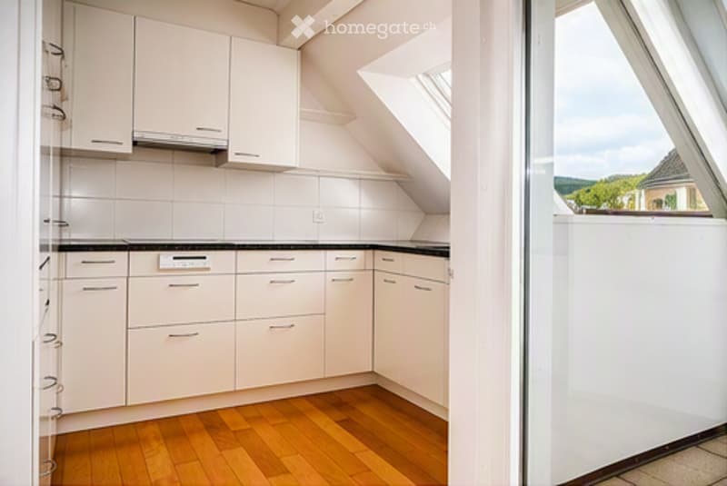 Modern kitchen with white cabinets, black countertops, and wooden flooring. Features a large window offering a view of the outdoors.