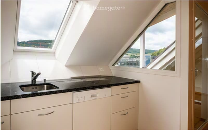 Bright kitchen with white cabinets, black countertop, stainless steel sink and faucet, and a dishwasher. Large windows offer a scenic view.