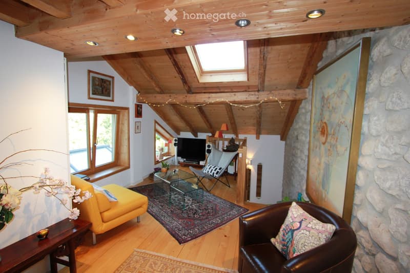 Cozy living room with wooden beams, exposed wooden ceiling, large windows, stone wall, yellow sofa, leather armchair, glass coffee table, TV, and decorative items.