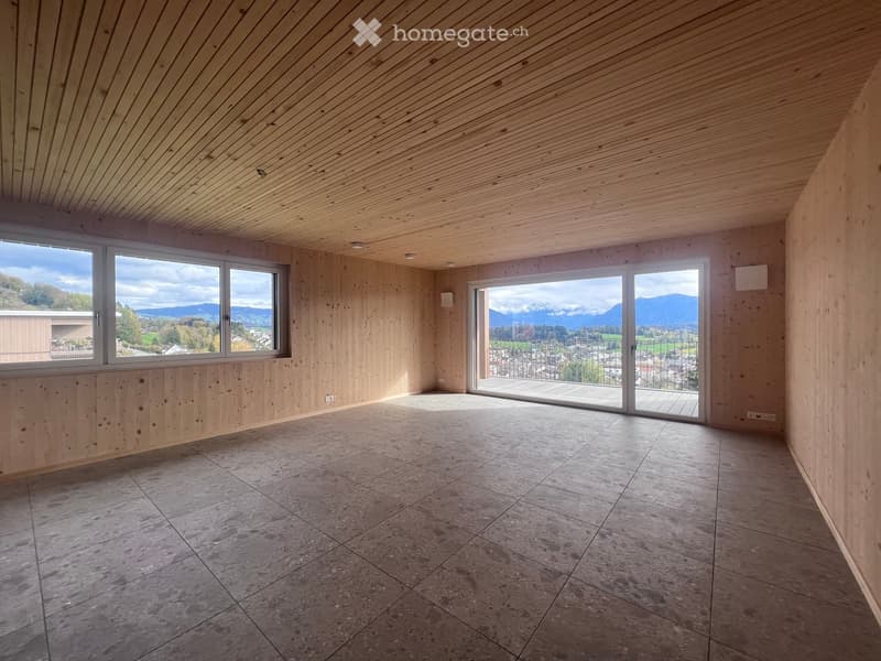 Empty room with wooden walls and ceiling, large windows, and a sliding glass door leading to a balcony with a scenic mountain view.