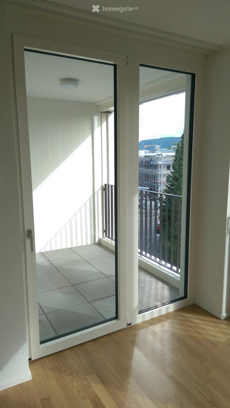 Modern interior with wooden flooring, large glass sliding doors leading to a balcony with metal railing and outdoor view.