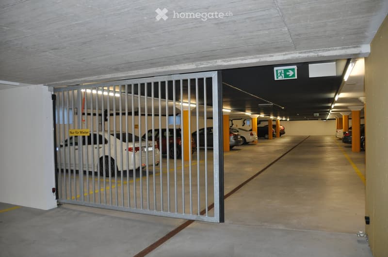 Underground parking area with several parked cars, marked parking spaces, and a security gate.