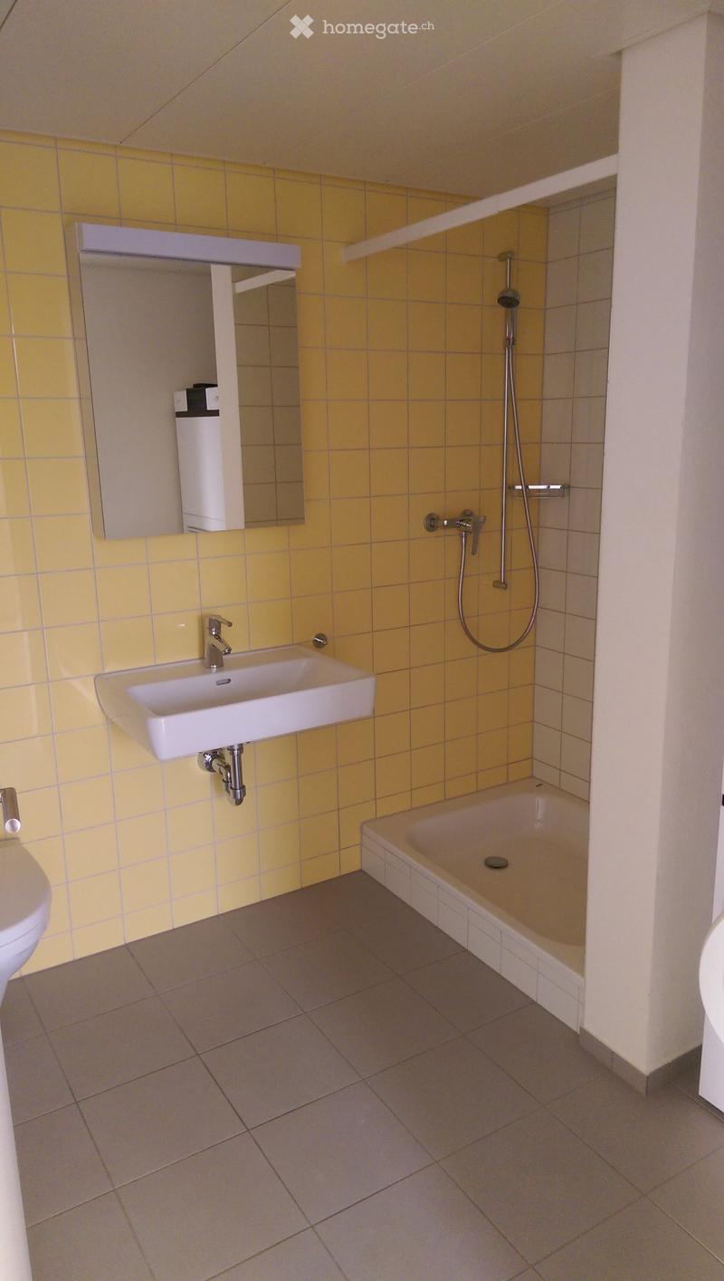 Modern bathroom with yellow tiled walls, a white sink, a bathtub, a showerhead, and a mirror above the sink.
