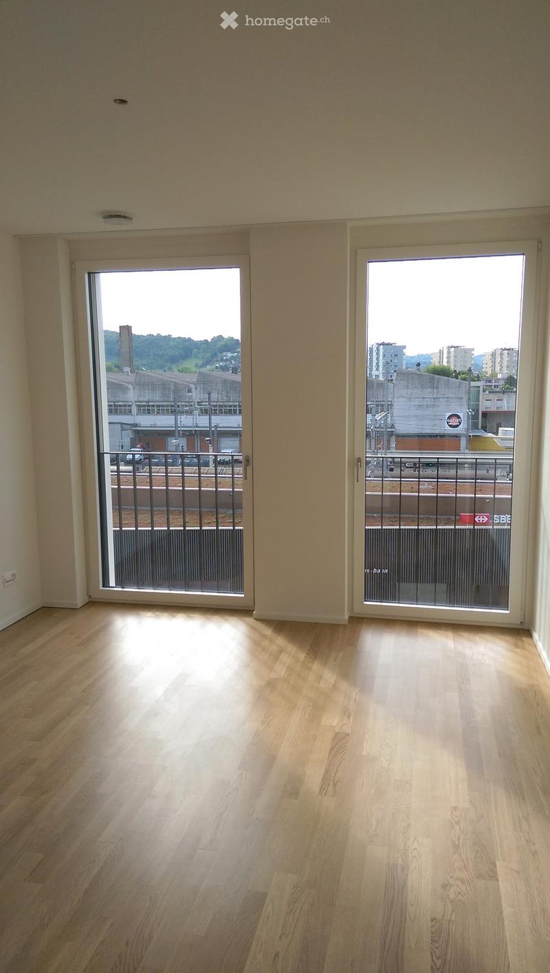 Empty room with light wooden flooring and two large sliding glass doors leading to a balcony with metal railings.