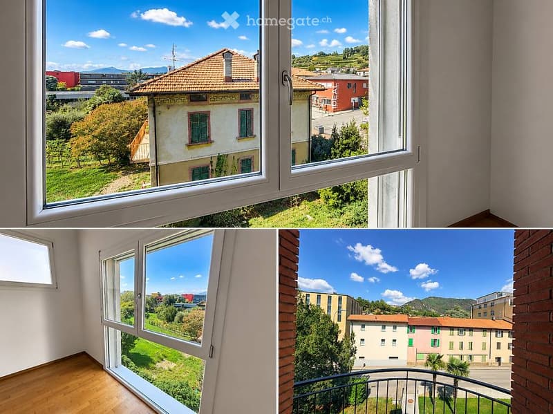 Empty room with large windows offering a scenic view of a town and surrounding greenery.