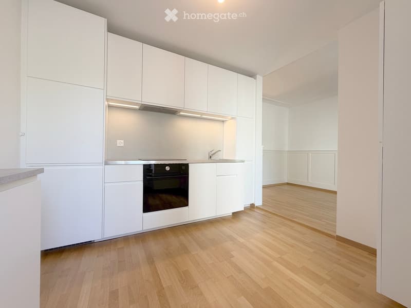 Modern, minimalist kitchen with white cabinets, a stainless steel oven, and a sink, featuring light wooden flooring and bright lighting.