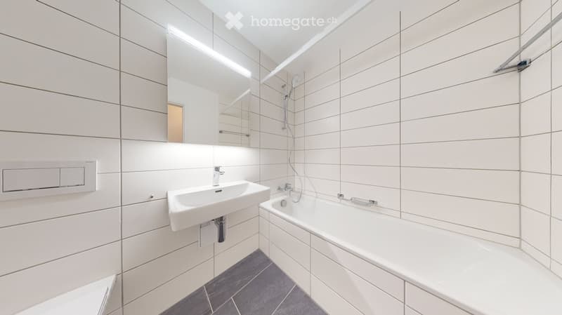 Modern bathroom with white tiles, a sink, bathtub, mirror, and showerhead.
