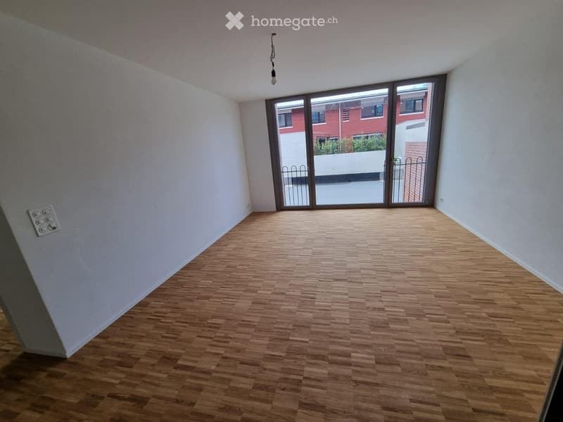 Empty room with wooden flooring, white walls, and large glass sliding doors leading to a balcony.